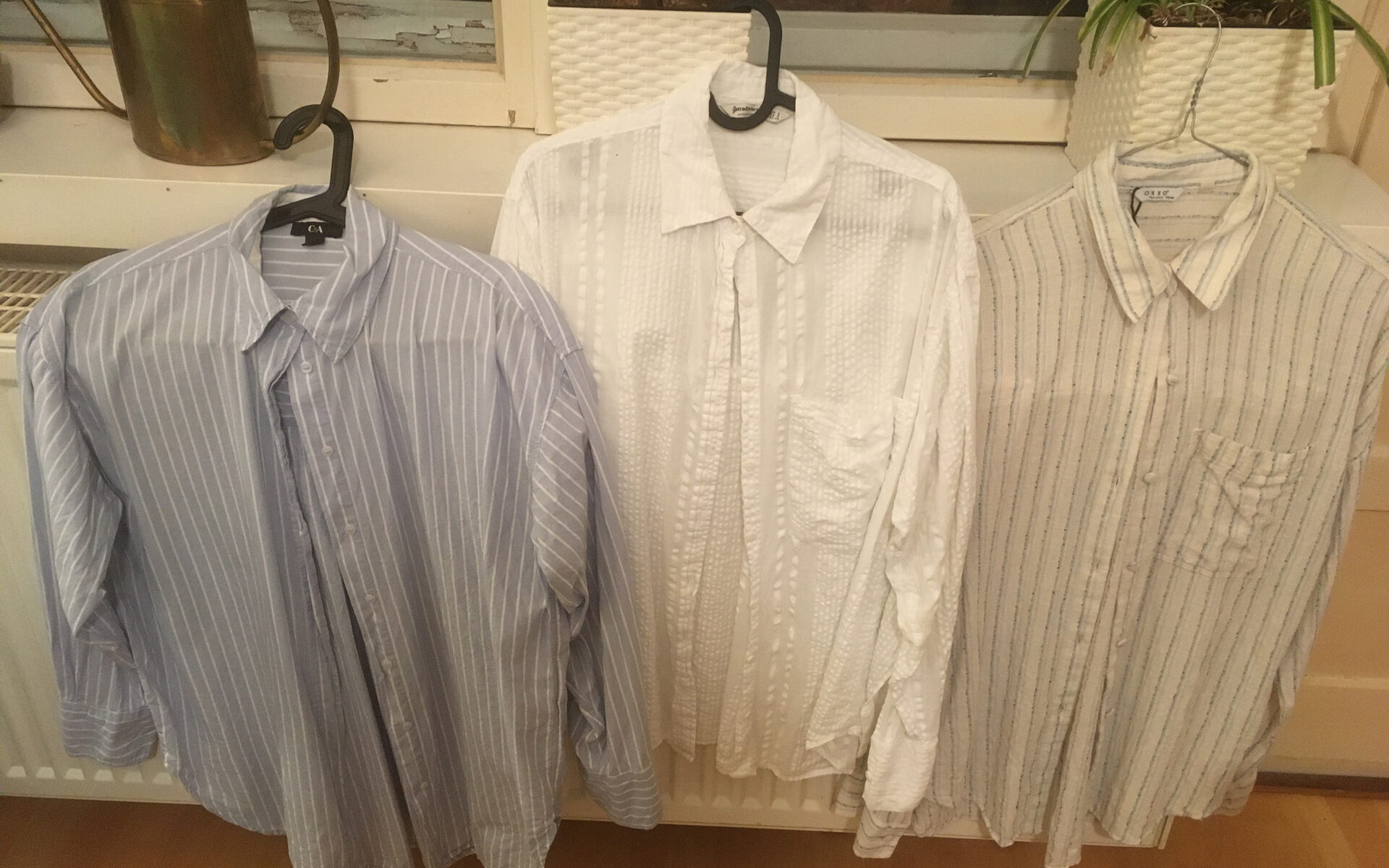 Drei Blusen auf Bügeln vor einer Heizung, zum Trocknen